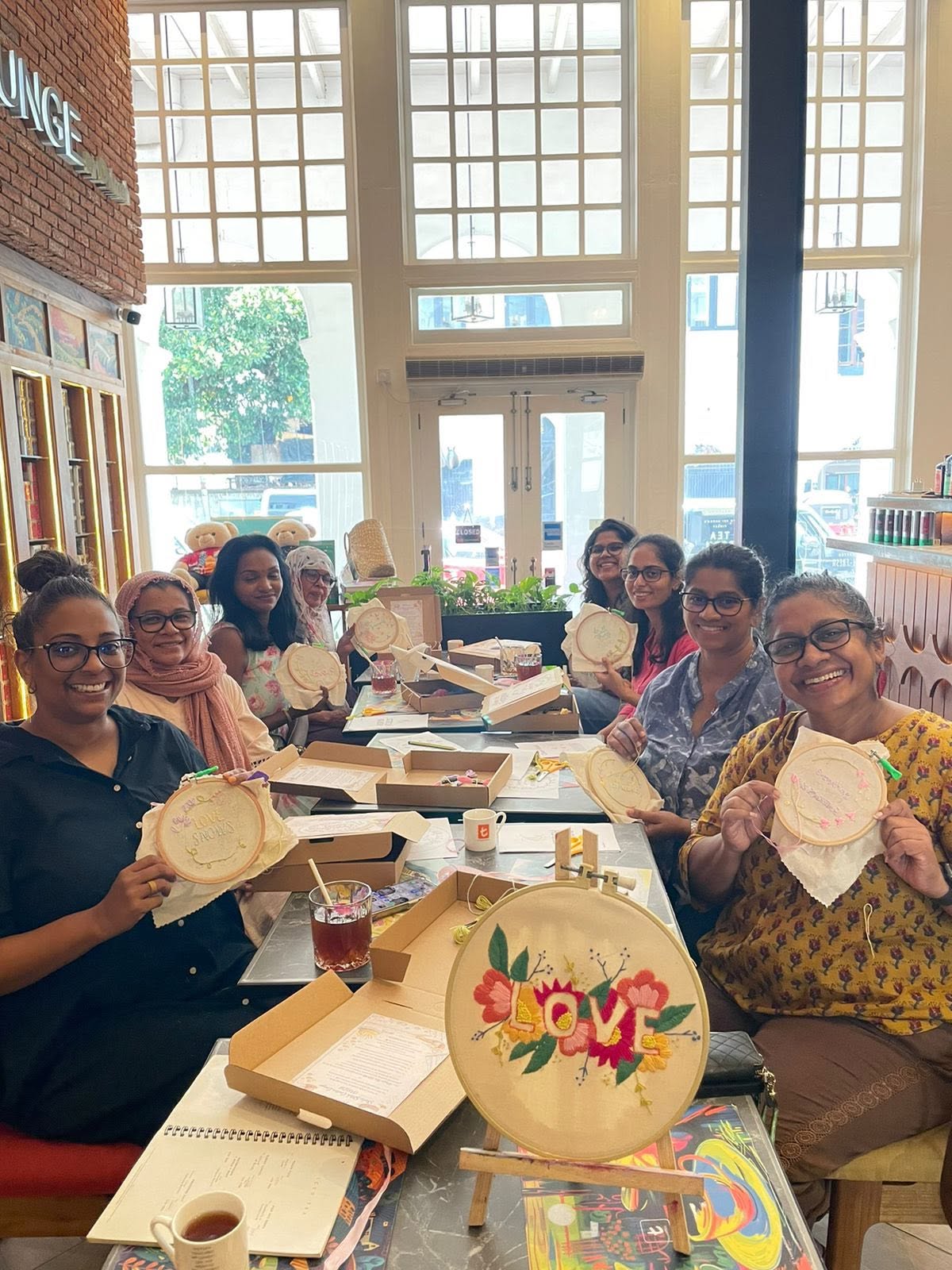 A group of adult students posing with their finished floral embroidery hoops at a Sewing Club workshop