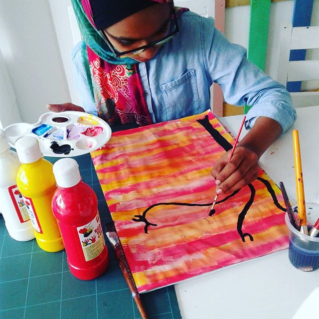 A teen in a headscarf mixing paint while working on a bright pink and orange canvas