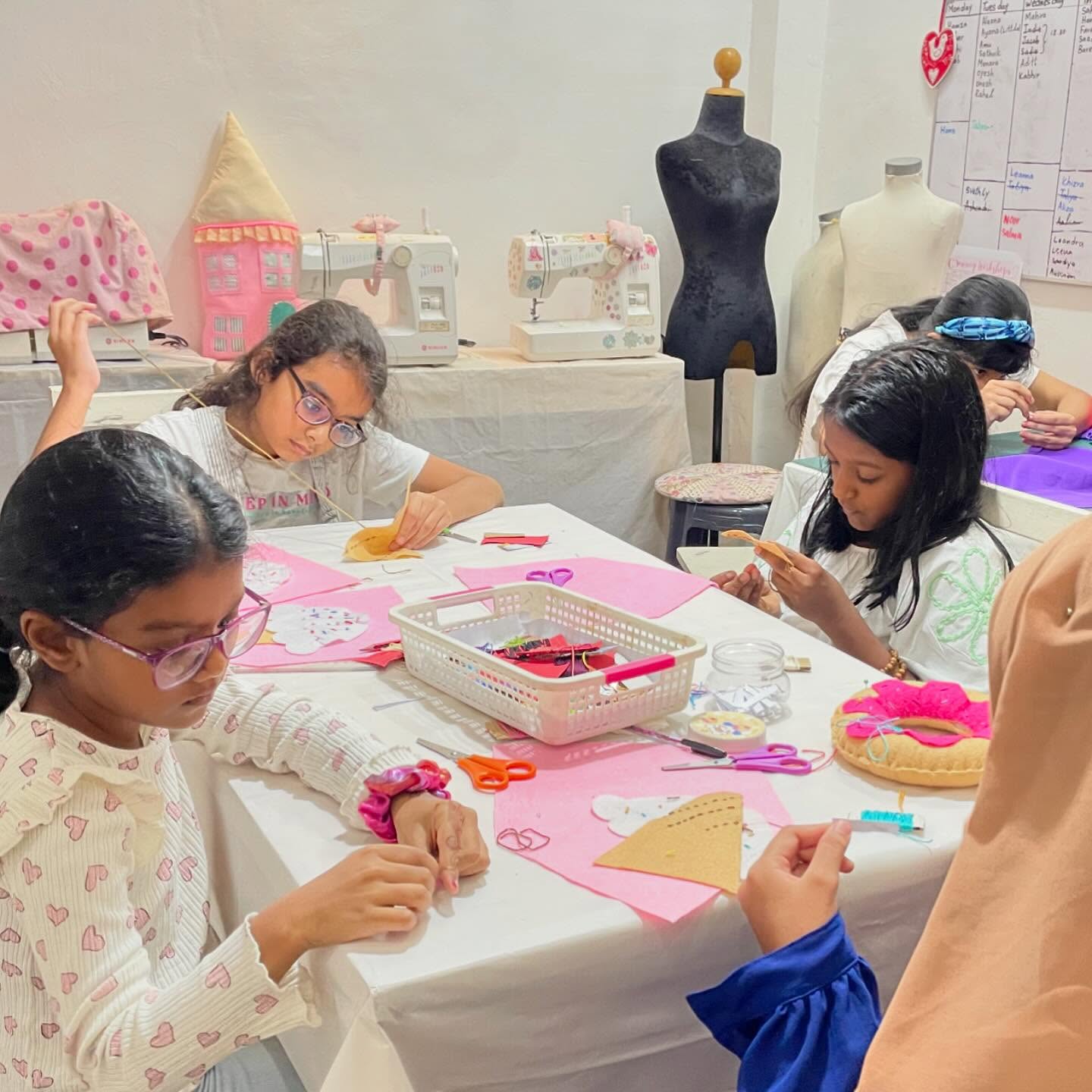 Kids sewing felt shapes at a table lined with sewing machines and dress forms
