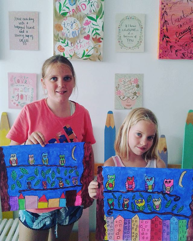 Two girls holding up matching hand-painted owl artworks