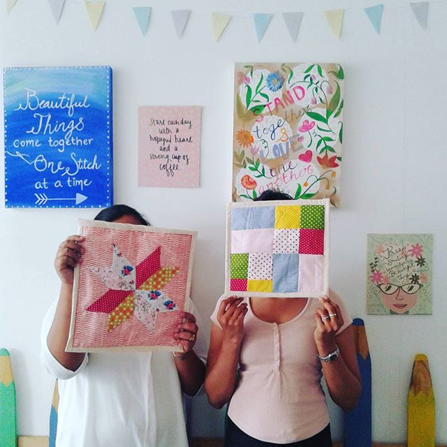 Two women holding up quilted patchwork squares they made in a sewing class