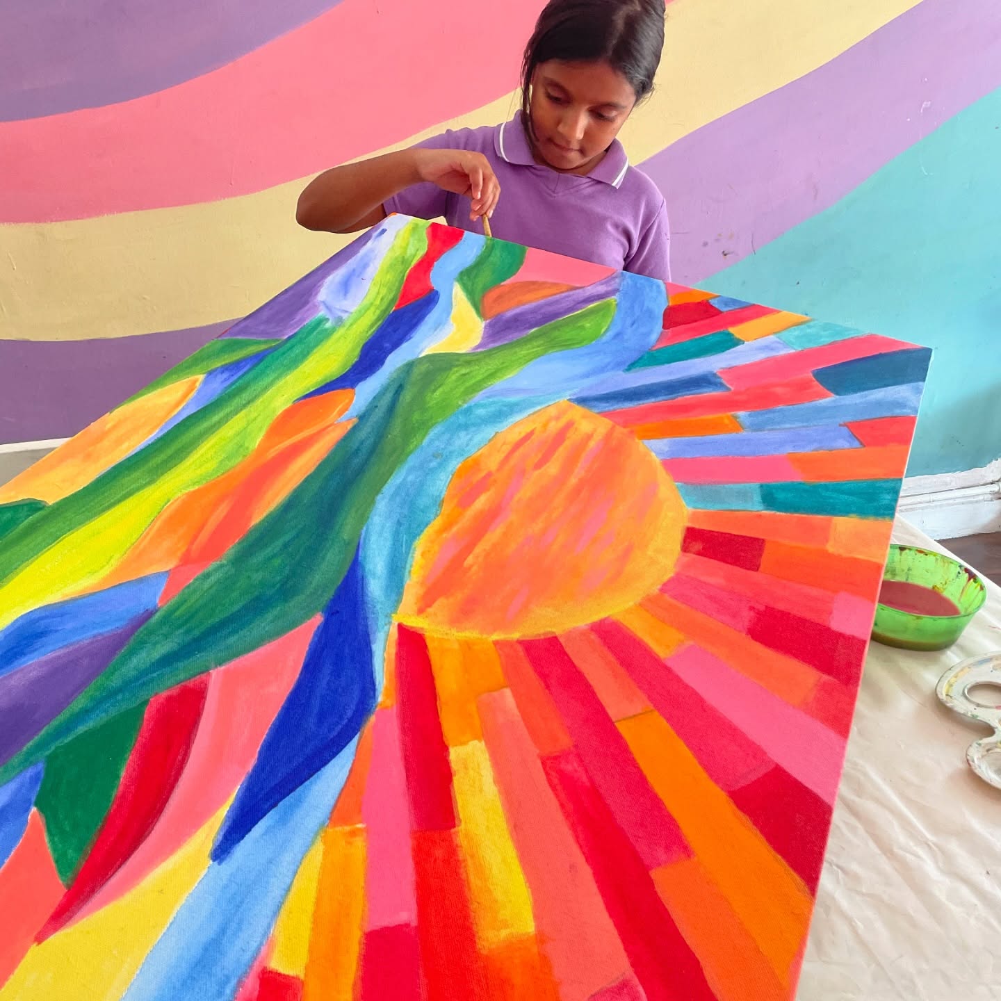 A girl in a school uniform painting a large rainbow sunburst canvas