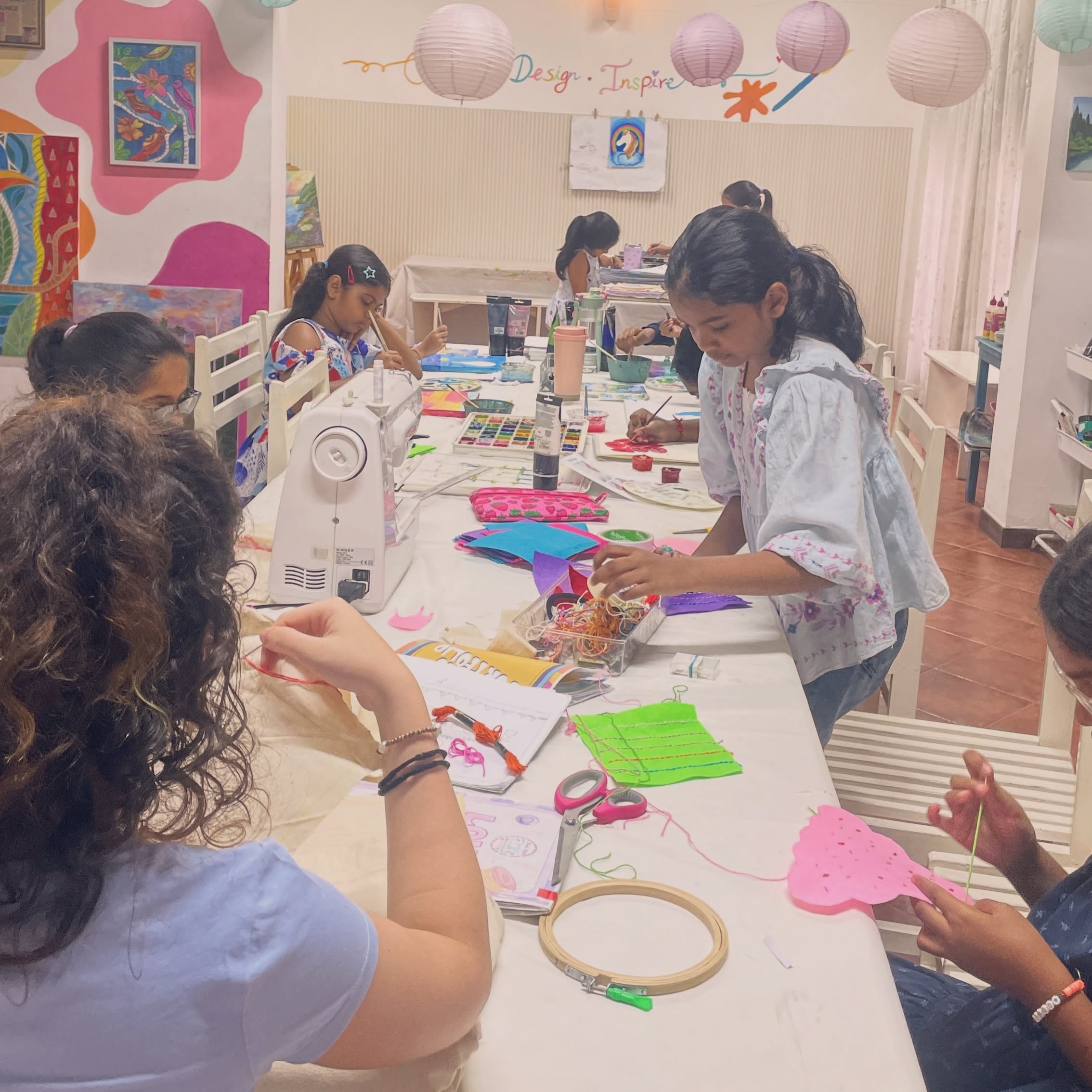Wide view of a busy Studio Stitch class, with kids painting, sewing machines, and an embroidery hoop on the table