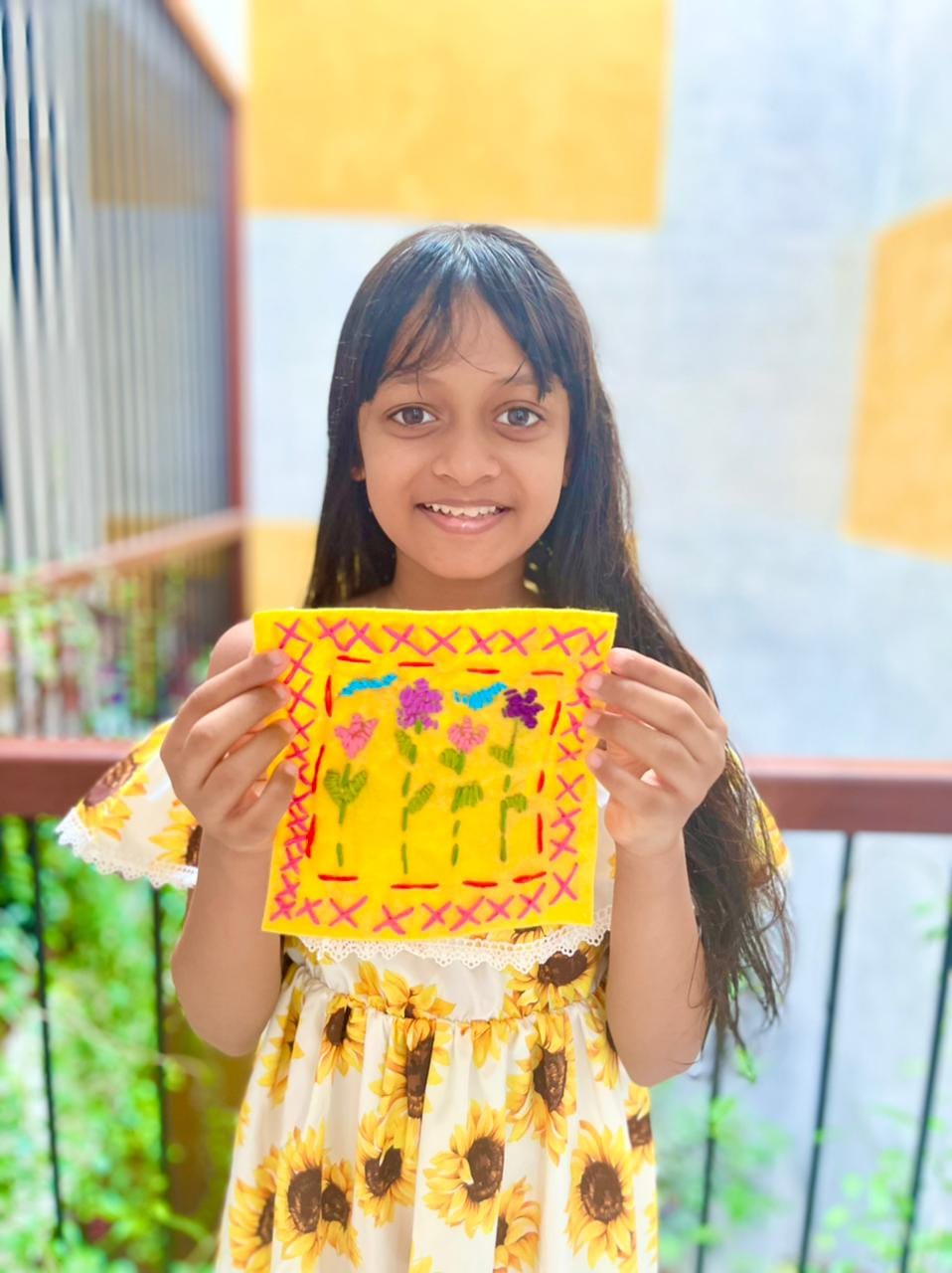 A girl in a sunflower dress holding her embroidered yellow felt patch