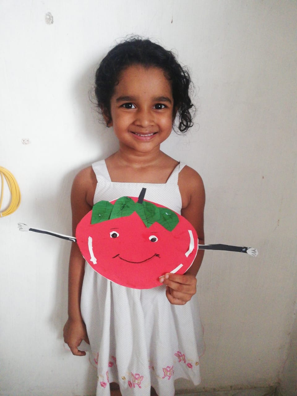 A girl holding up her handmade smiling tomato character craft