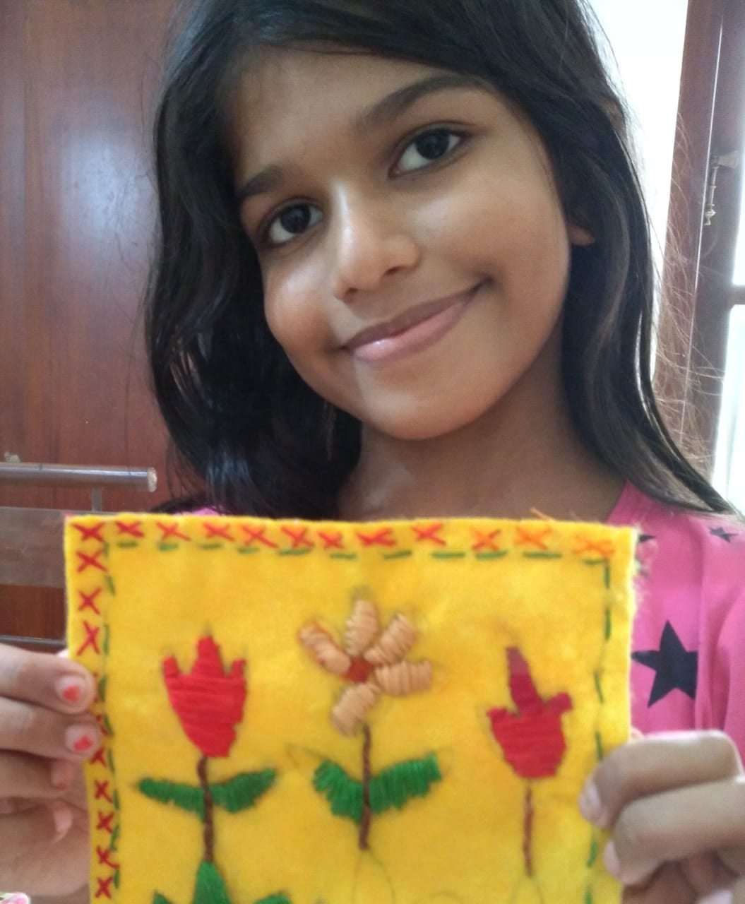A close-up of a girl holding her embroidered felt piece with red flowers